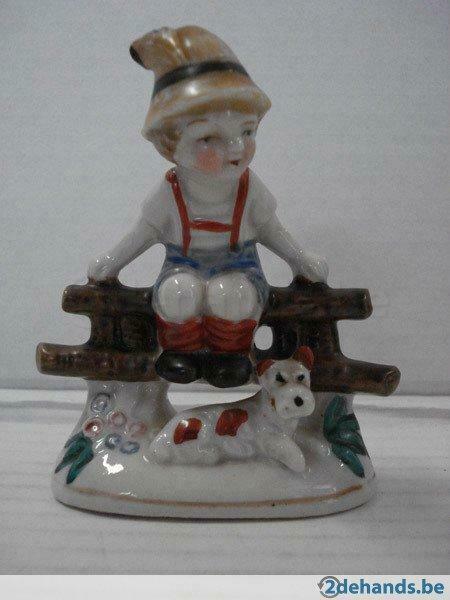 Porselein: Tiroler jongen zittend op hek met hond erbij.